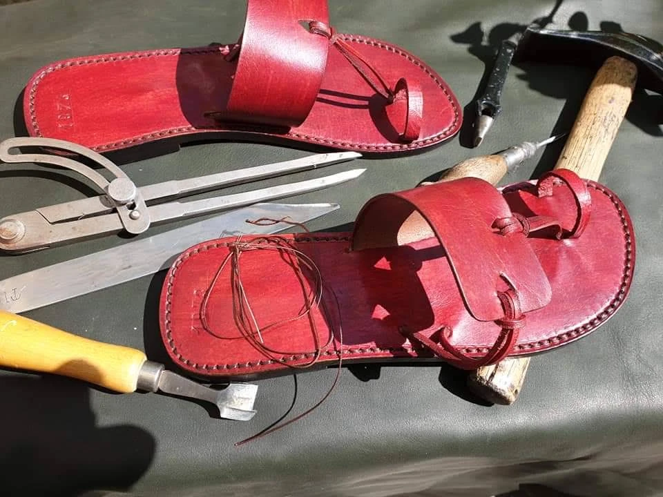 Rote Ledersandalen, Nähfaden und Schuhmacherwerkzeuge auf einer Werkbank, fotografiert von Cvetan Varadinov